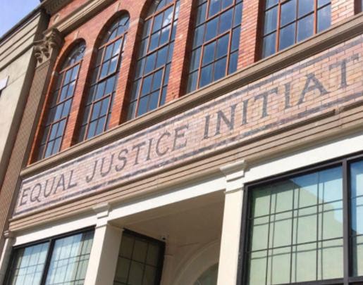 Small version of brick wall with phrase 'Equal Justice Initiative' painted on it bellow a row of windows for mobile