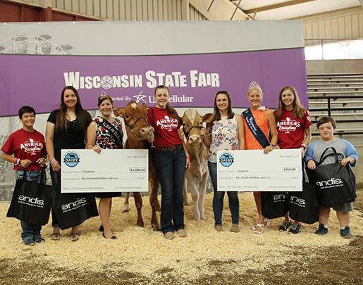 Small version of Six winners, two presenters and two cows standing in front of a Wisconsin State Fair banner at award ceremony with giant novelty checks and Andis tote bags