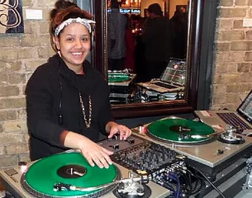 Small version of high-school age girl standing at DJ turn tables spinning a green record and smiling at camera for mobile