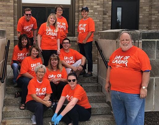 Large version of group of 11 Andis associates sitting on steps in front of a school all wearing orange Day of Caring T-shirts